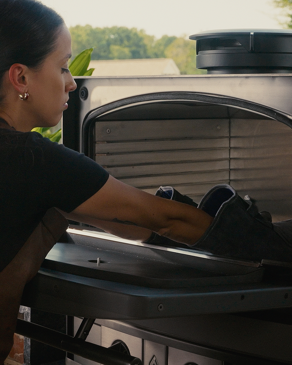 A chef loads charcoal within the Emberhaus Fire Oven, demonstrating its spacious live-fire design and ember versatility in an elegant outdoor kitchen setting.