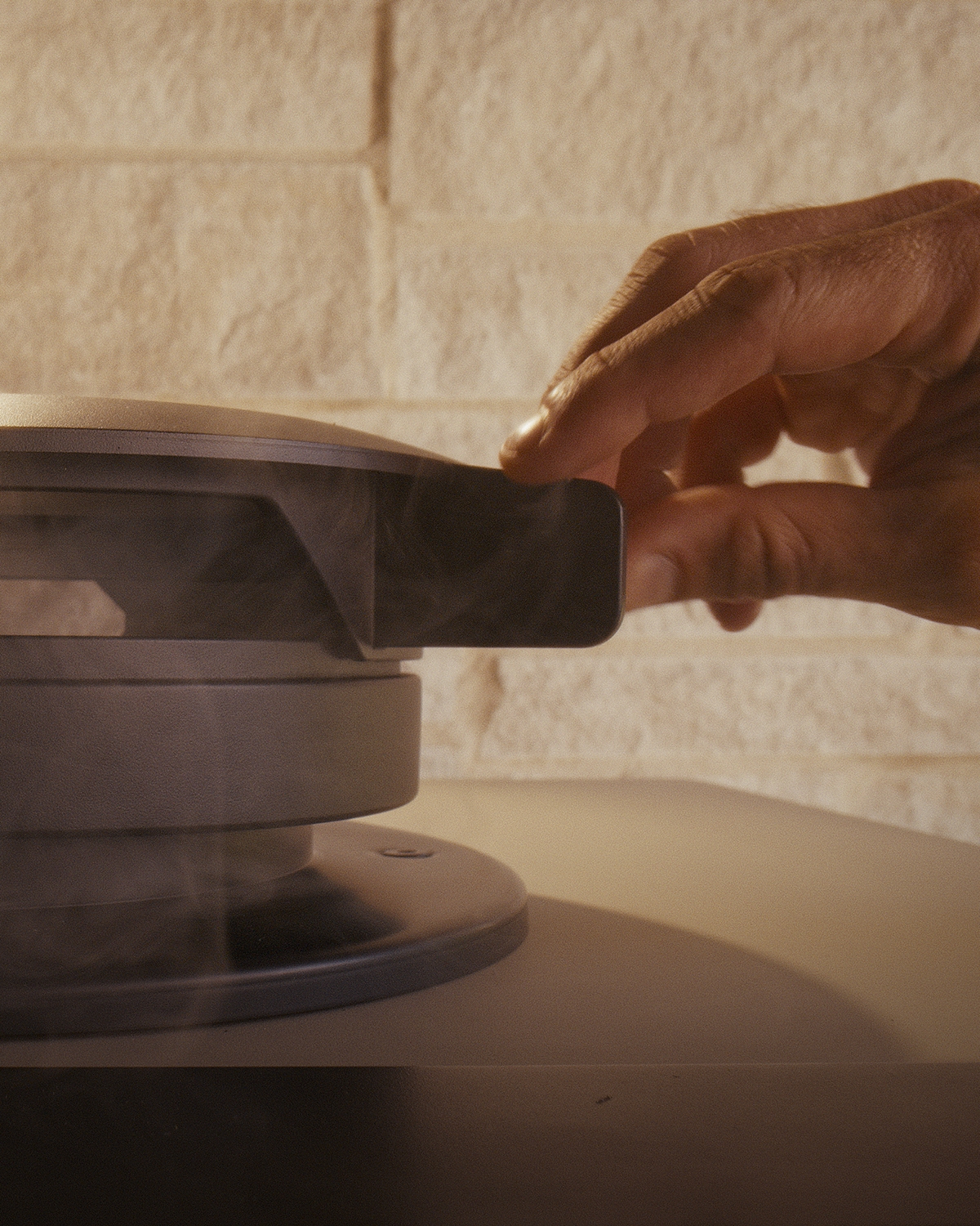 A hand adjusts the Emberhaus Emberflow Vent atop the Fire Oven, with smoke rising gracefully—showcasing the precision airflow control and refined engineering behind Emberhaus live-fire cooking.