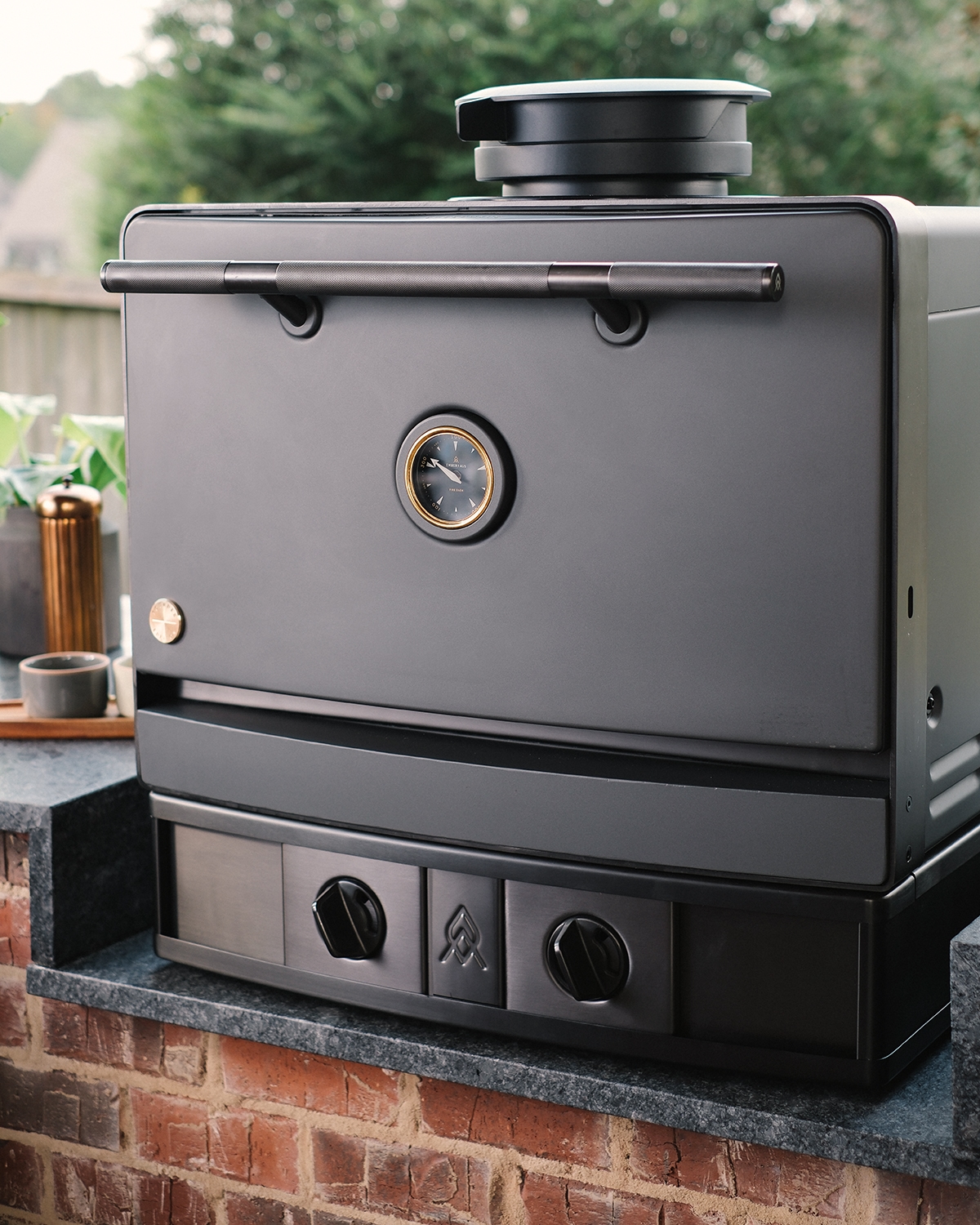 The Emberhaus Fire Oven displayed in an elegant outdoor kitchen, showcasing its matte Iron finish, brass detailing, and precision craftsmanship—designed for luxury live-fire cooking.
