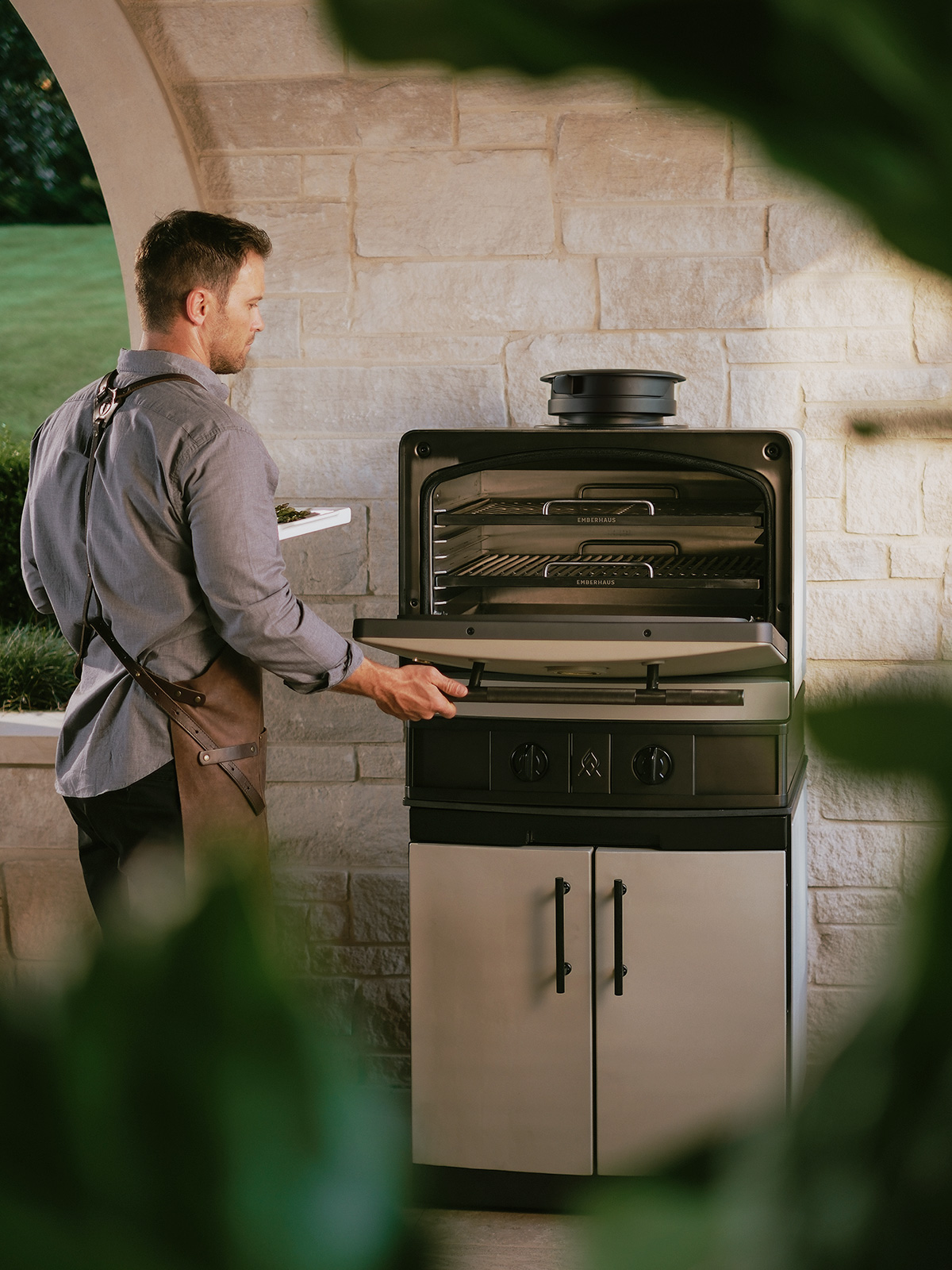 Man opening the Emberhaus Fire Oven in a luxury outdoor kitchen, highlighting premium design, live-fire craftsmanship, and built-in cabinetry.