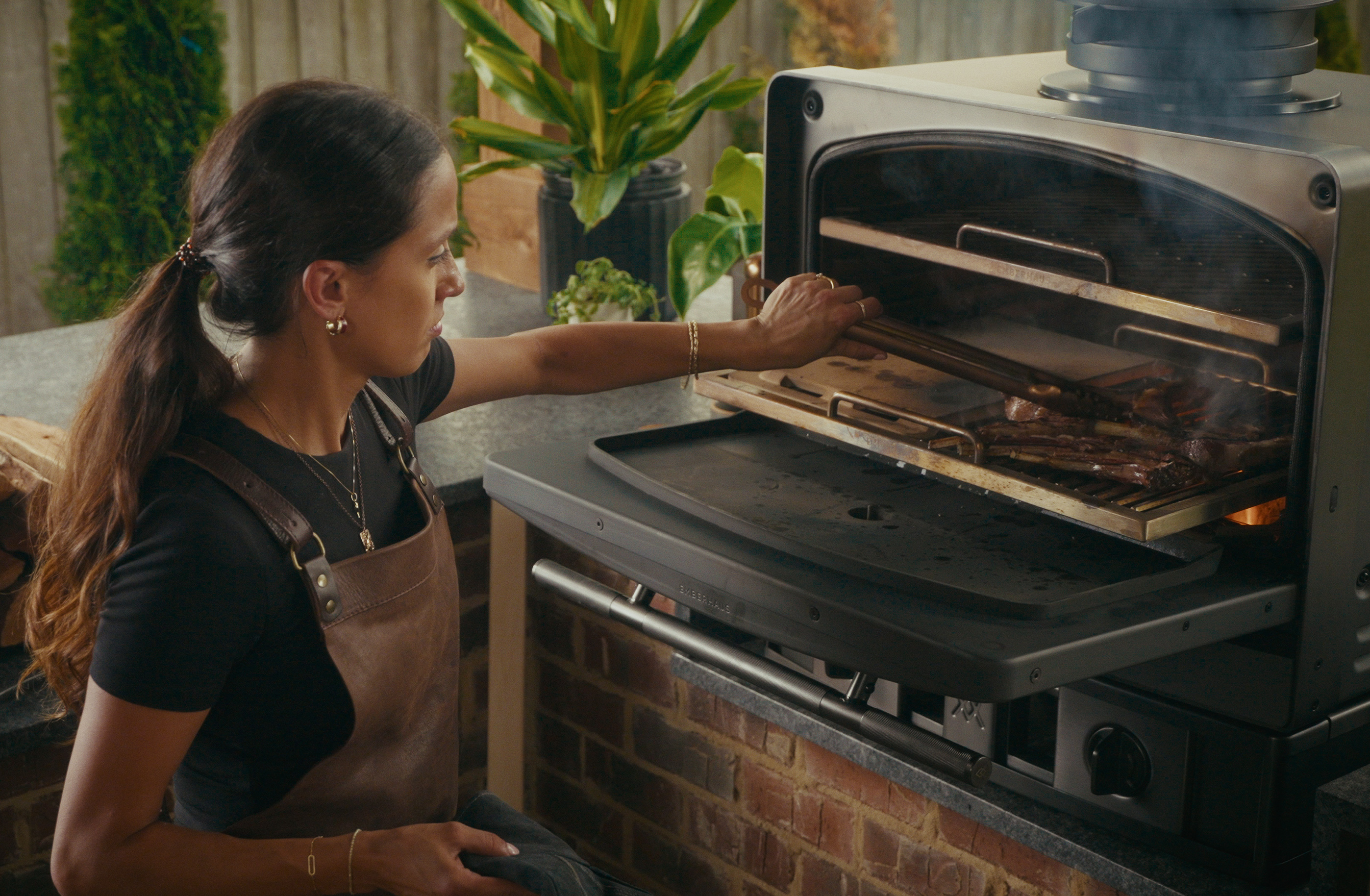 Female chef grilling meat in an Emberhaus Fire Oven, showcasing open-flame cooking, precision control, and luxury outdoor kitchen craftsmanship.