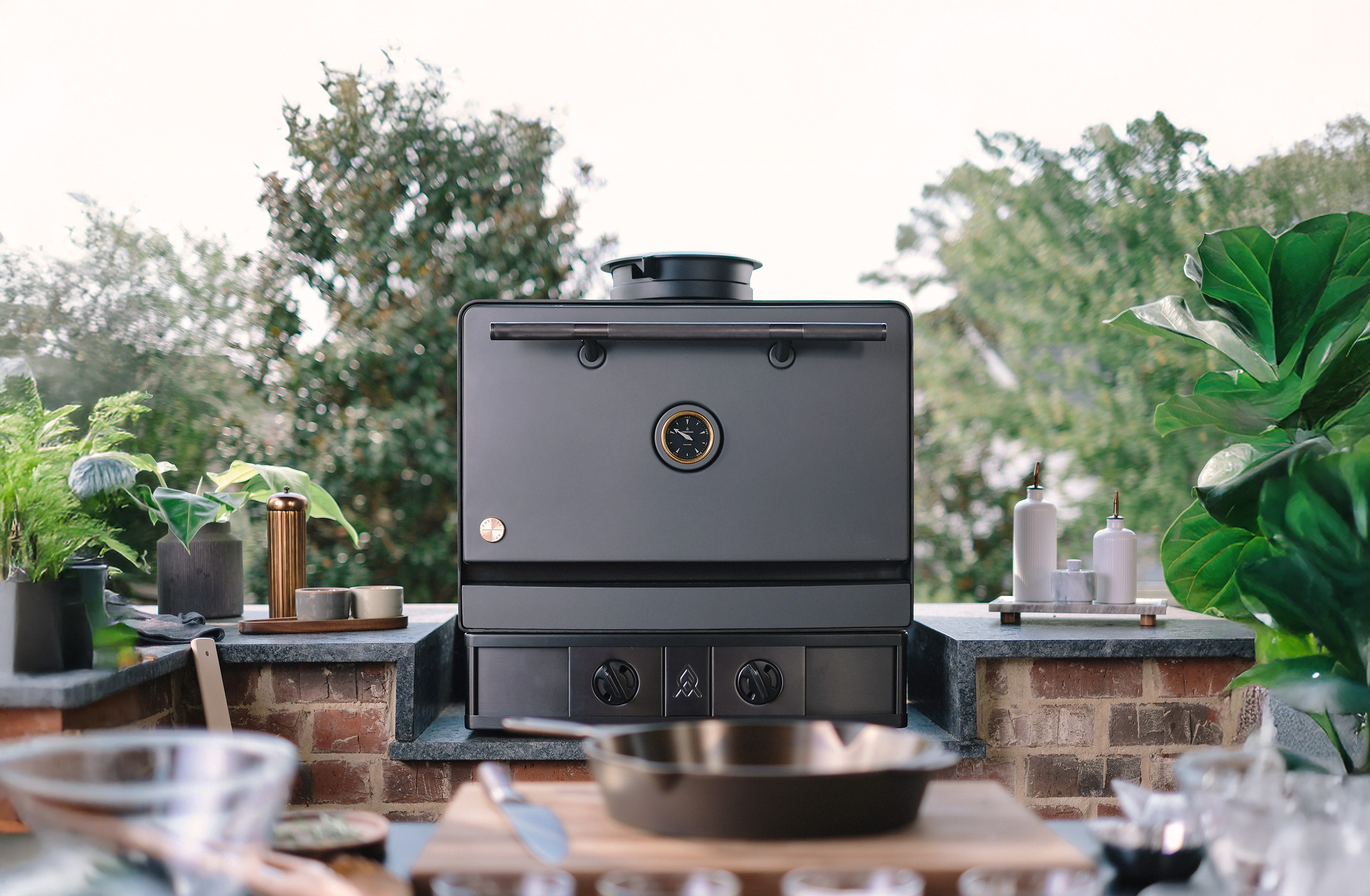 Emberhaus Fire Oven in Iron color with Dark PVD Trim installed in an outdoor kitchen with black countertops and natural brick.